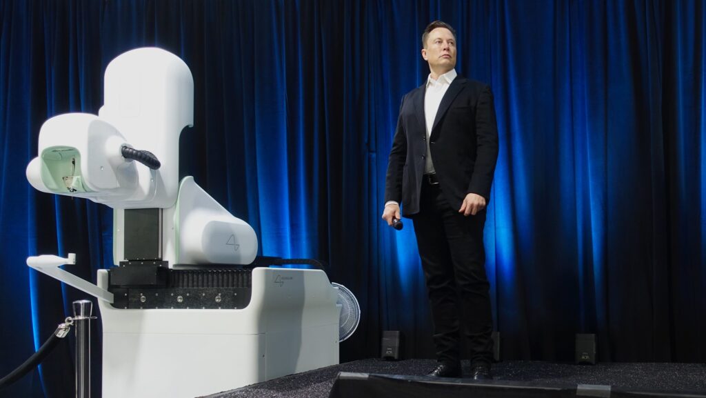 Elon Musk stands next to Neuralink robot device