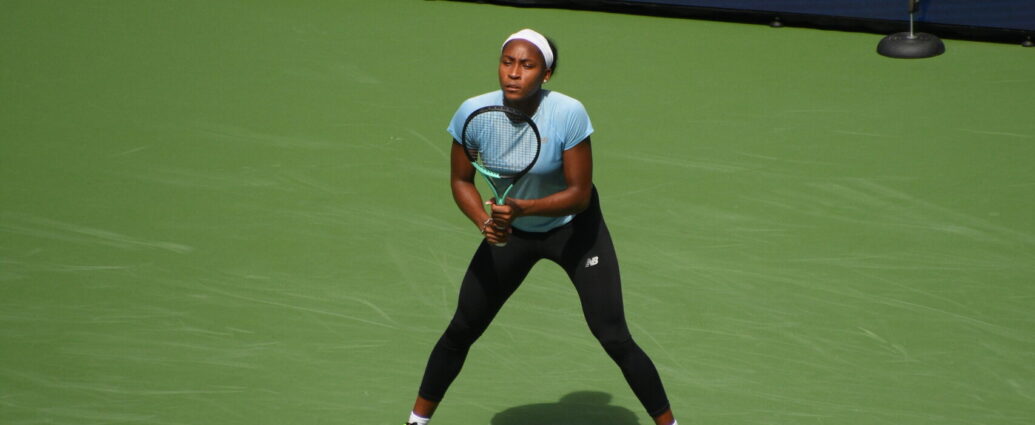 Coco Gauff on a tennis court wearing a blue t-shirt and black sports leggings.