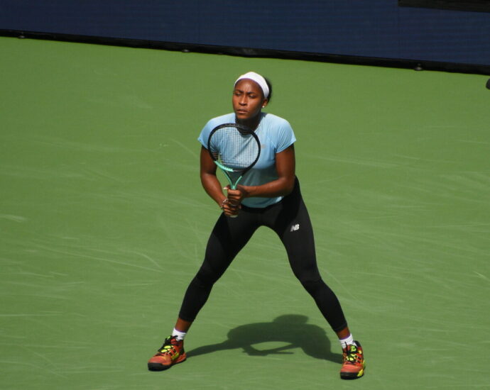 Coco Gauff on a tennis court wearing a blue t-shirt and black sports leggings.