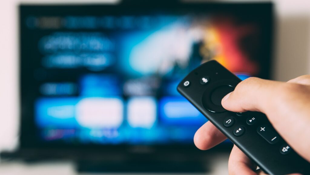Person holding a remote control towards a blue television screen.