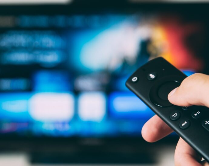 Person holding a remote control towards a blue television screen.