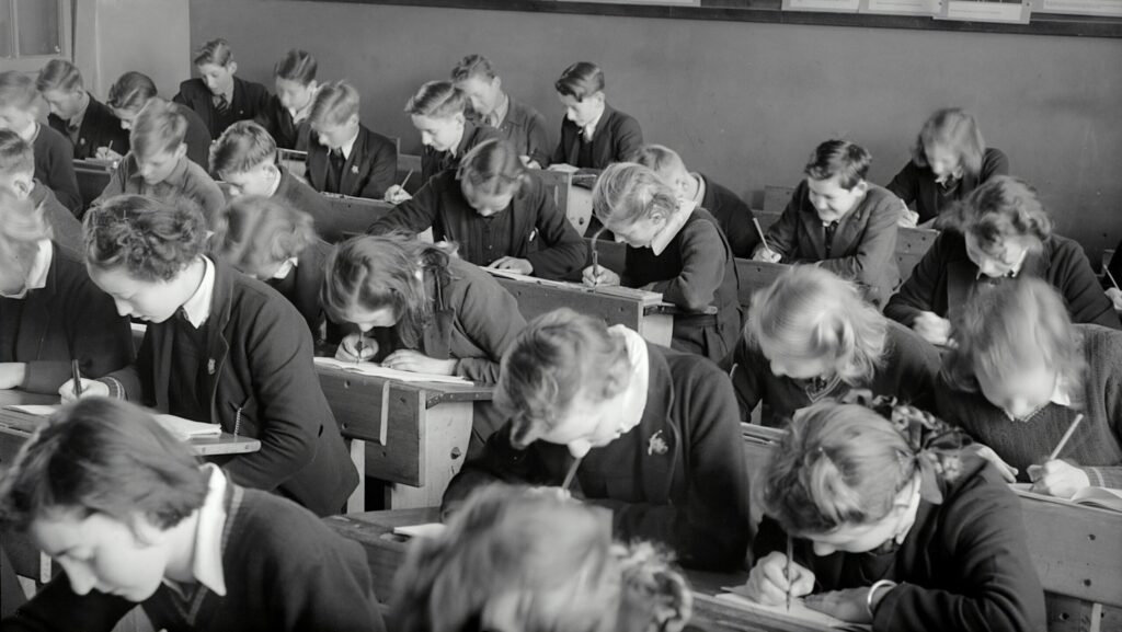 A black and white image of a classroom of school children wearing uniform.