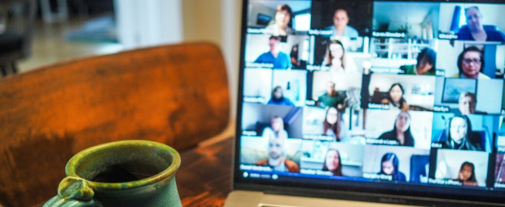 a laptop screen displaying a team video call next to a mug
