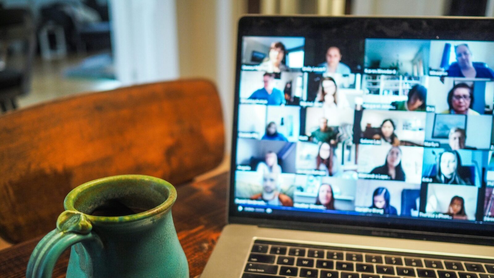 a laptop screen displaying a team video call next to a mug