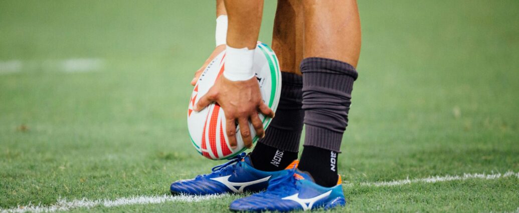 Scotland England. man wearing blue rugby boots holding rugby ball above togs.