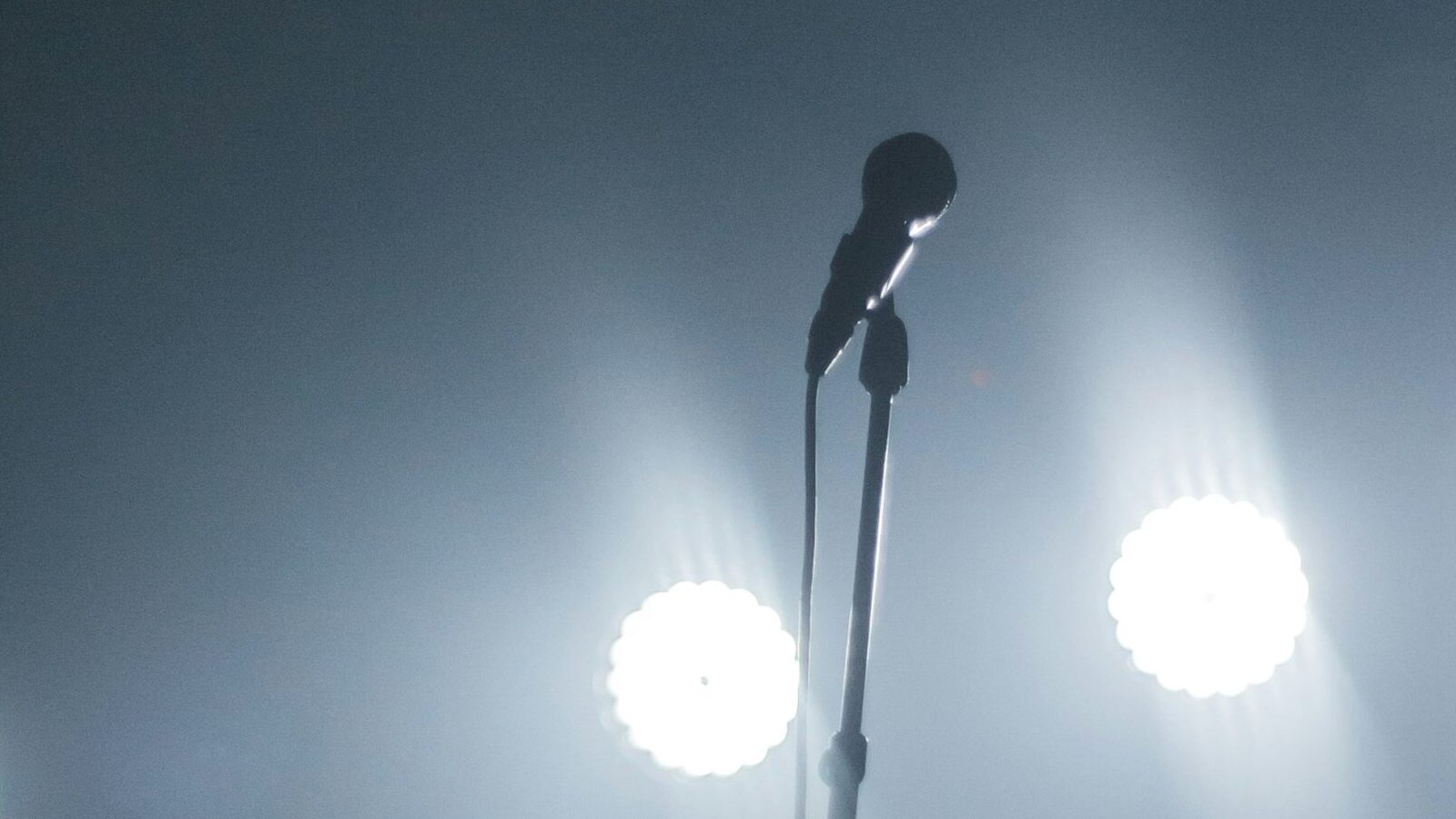 Image shows a microphone under stage lights [Touring]