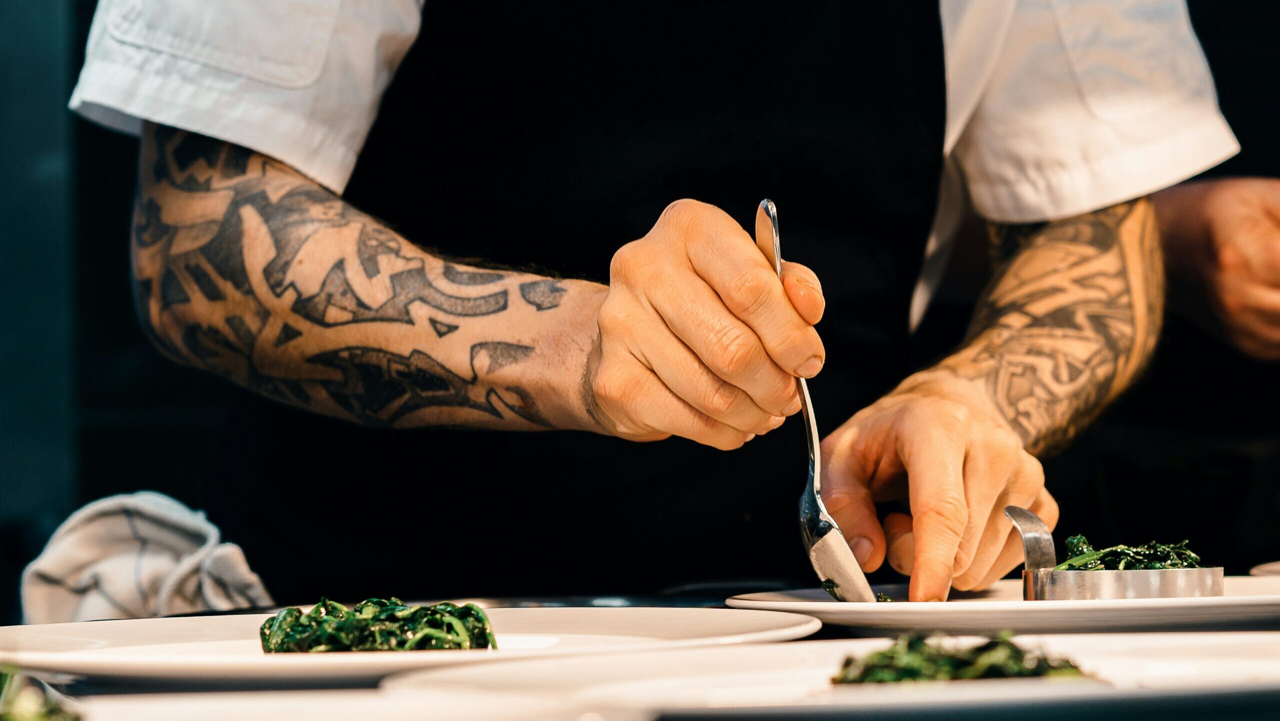 tattooed chef's arms plating up dish