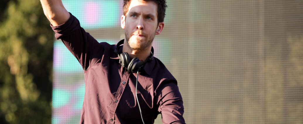Calvin Harris doing a DJ set at a festival with one hand up in the air, 2012.