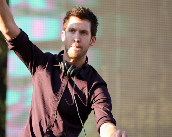 Calvin Harris doing a DJ set at a festival with one hand up in the air, 2012.