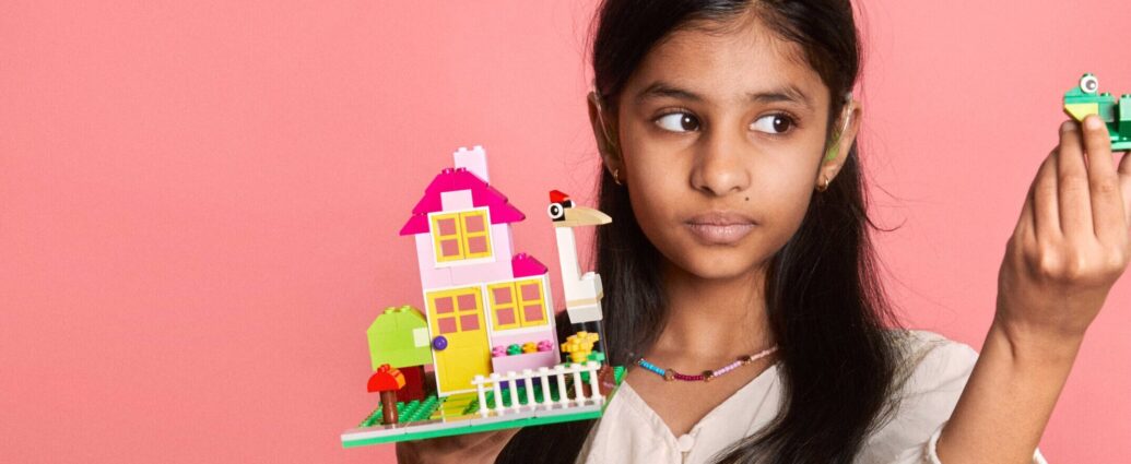 girl holding a lego house against a pink backdrop
