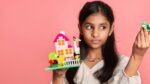 girl holding a lego house against a pink backdrop