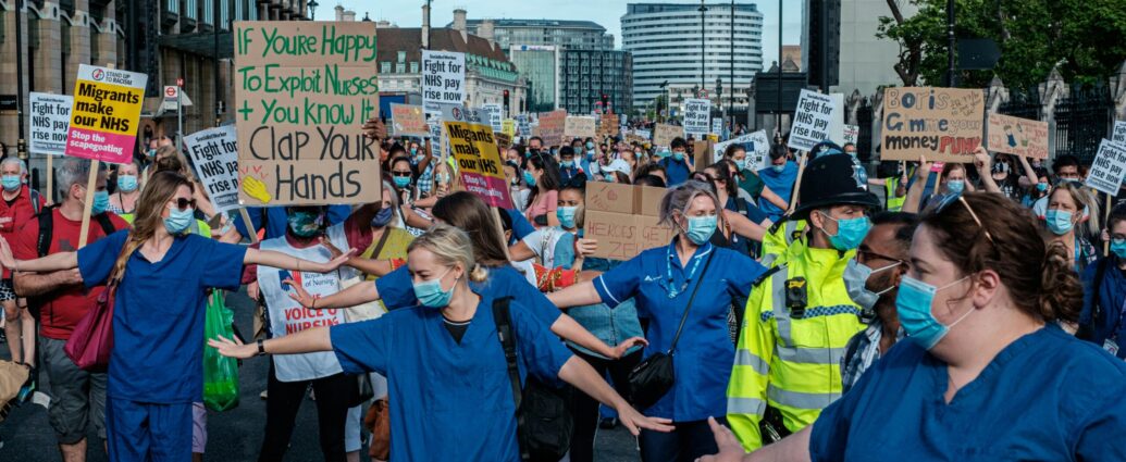 Nurses in blue scrubs and face masks standing with their arms outstretched in the middle of the road during NHS strikes