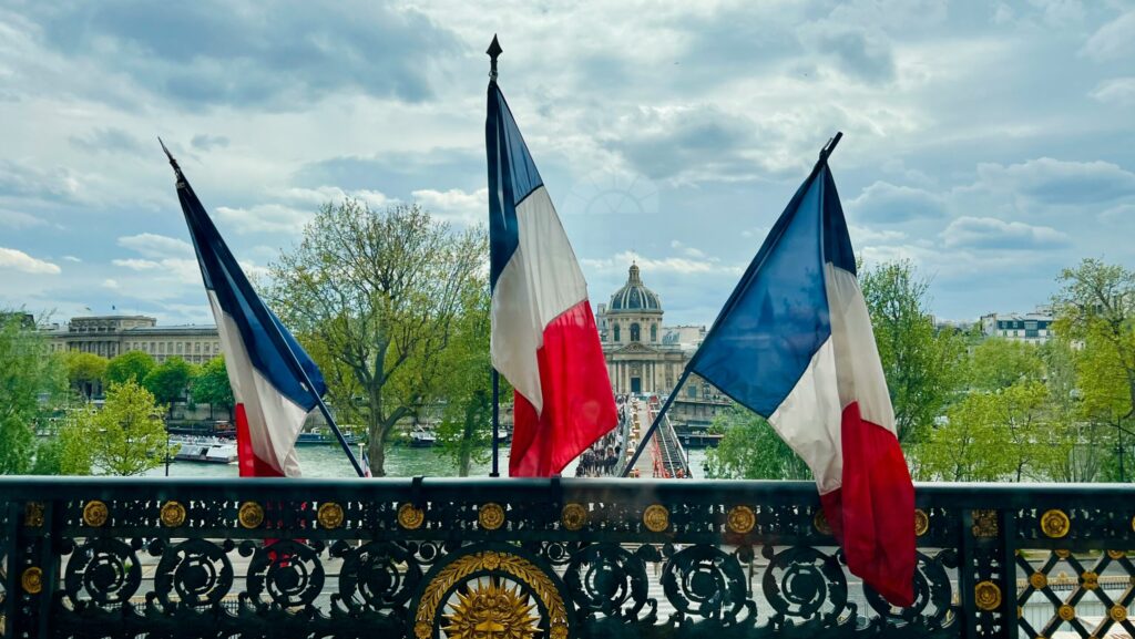 Three french flags sit upright from a balcony overlooking Paris.