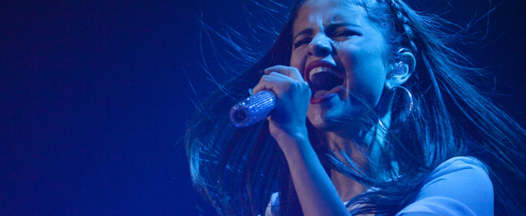 Selena Gomez singing with emotion into a microphone.