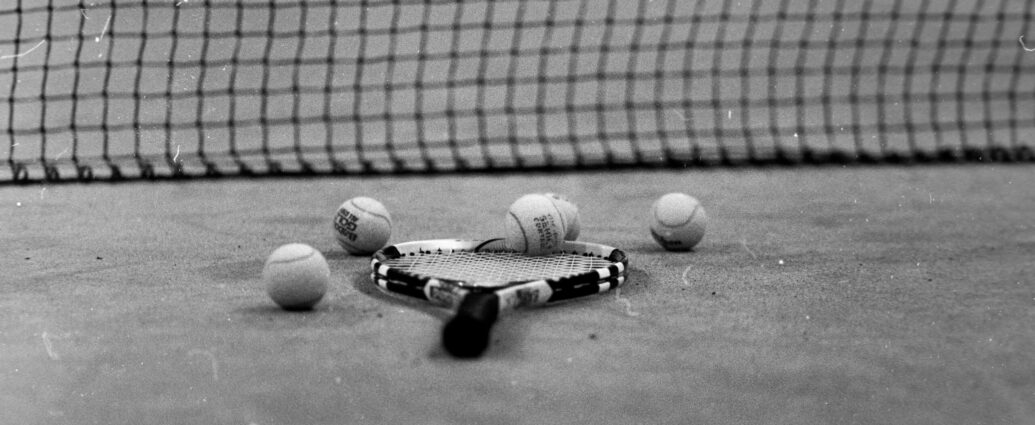 Black and white picture of a tennis racket lying on the ground surrounded by tennis balls.