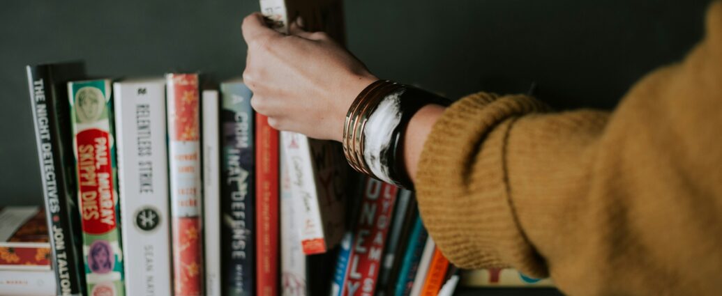 Person picking books from bookshelf