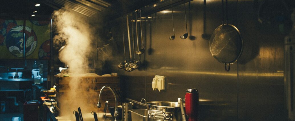 An industrial kitchen with large pots cooking on the stove.
