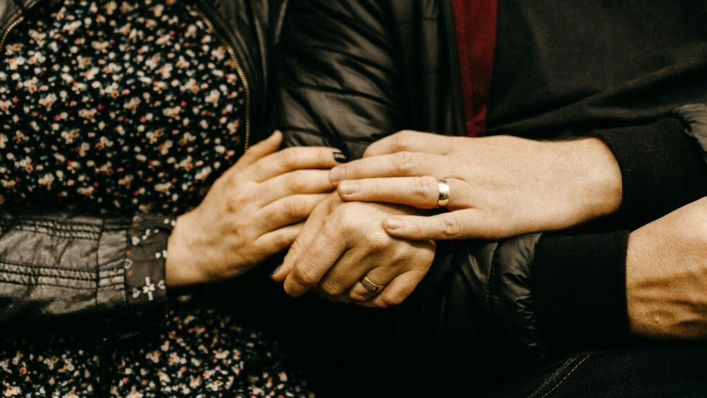 A man and woman holding hands, wearing wedding rings.