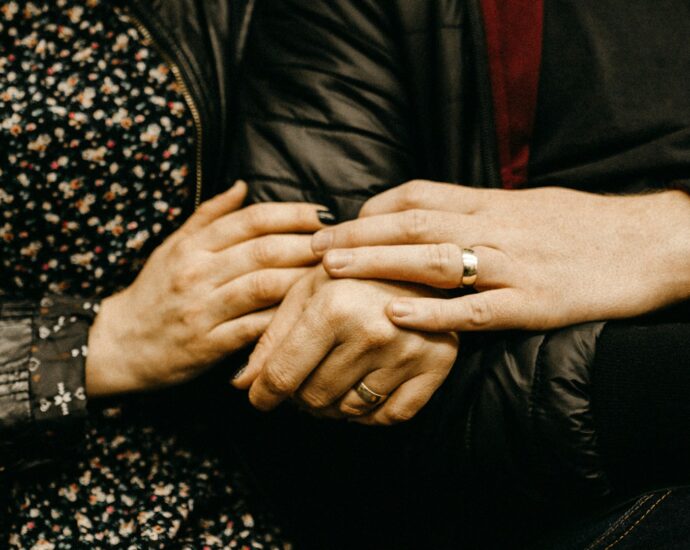 A man and woman holding hands, wearing wedding rings.